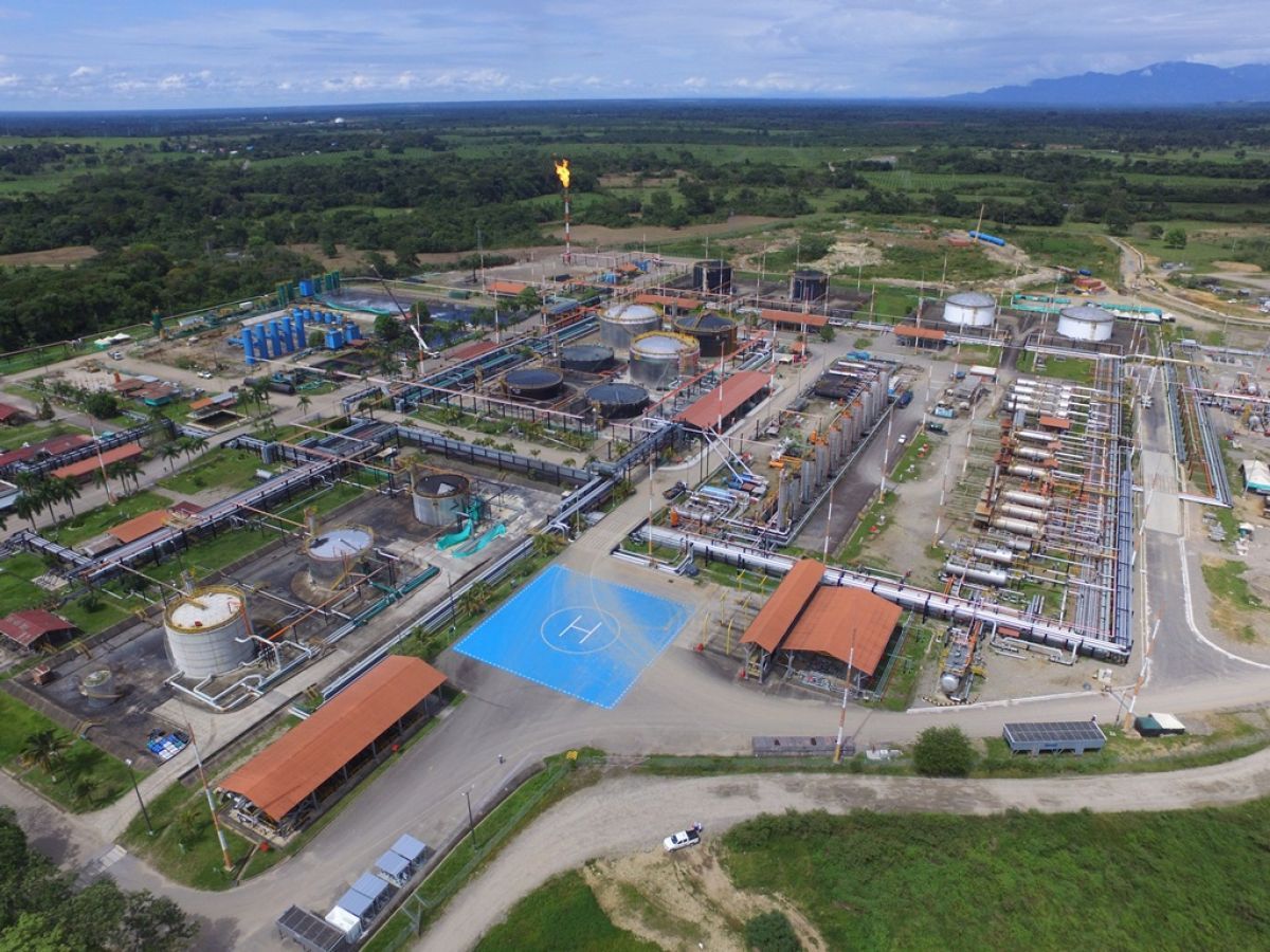 Vista aérea de una refinería de petróleo con tanques de almacenamiento, tuberías y un helipuerto en un paisaje rural verde.