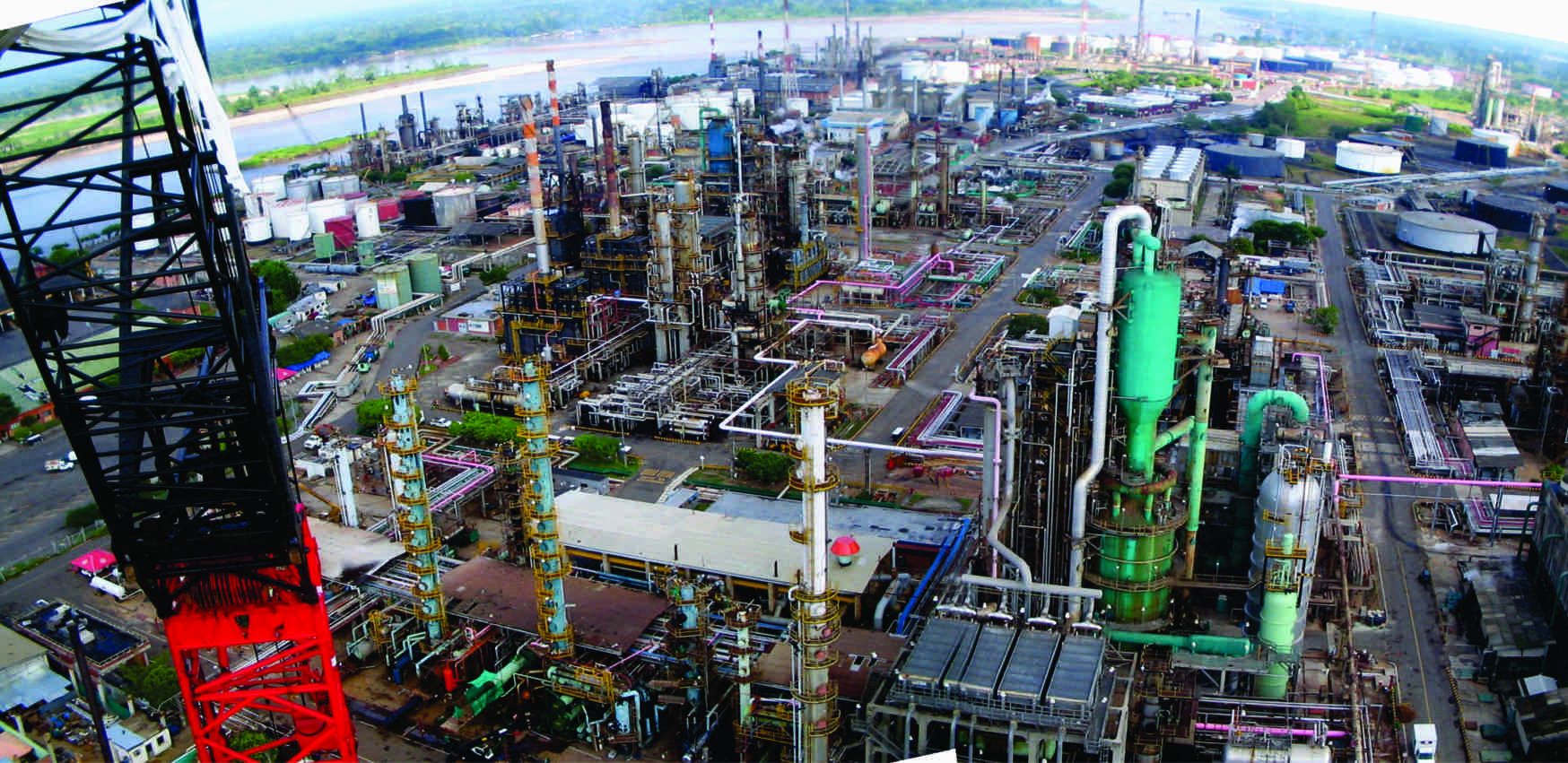 Vista aérea de un complejo industrial con estructuras altas y cilíndricas, tuberías y una grúa.