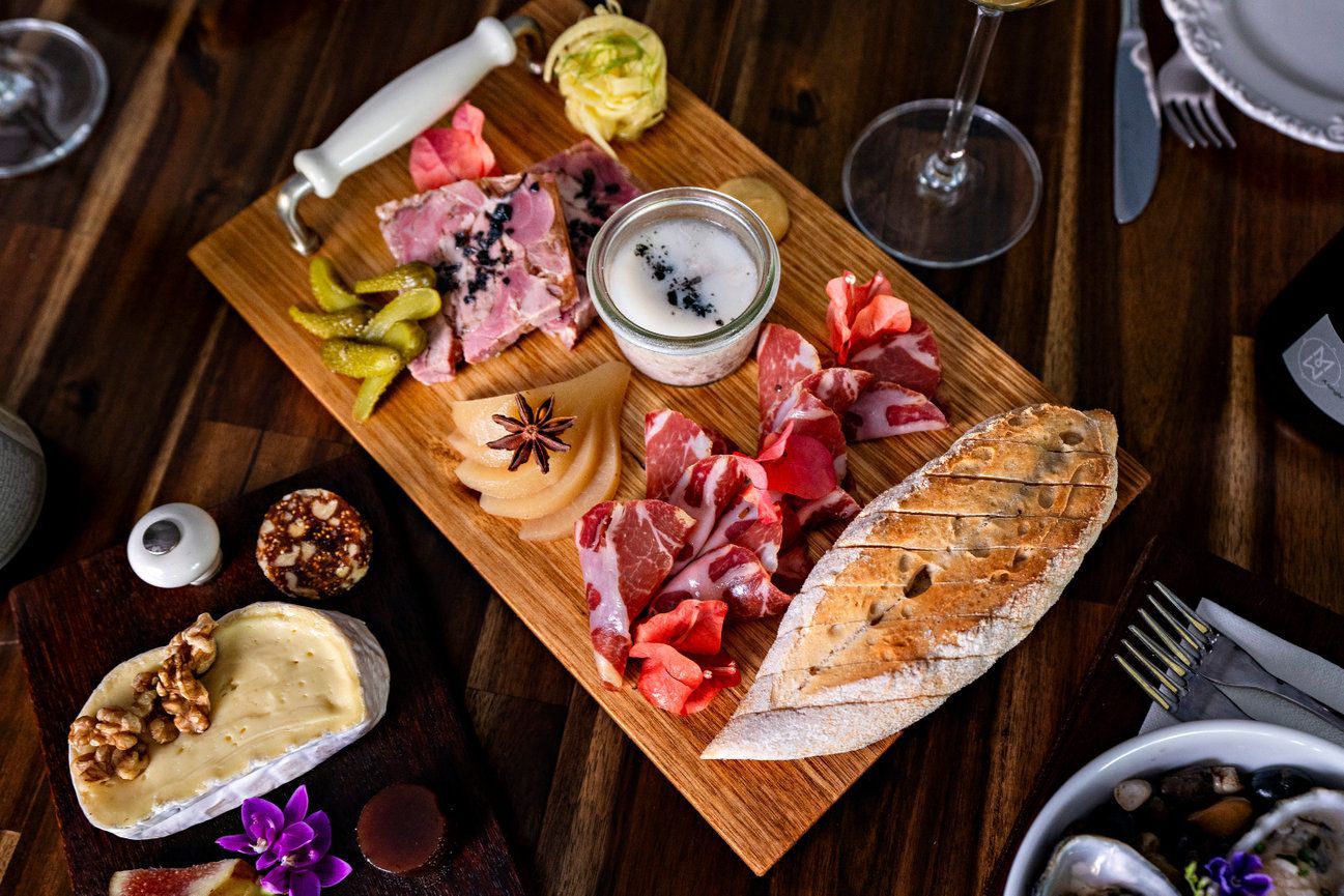 A wooden cutting board filled with meat and cheese on a wooden table.