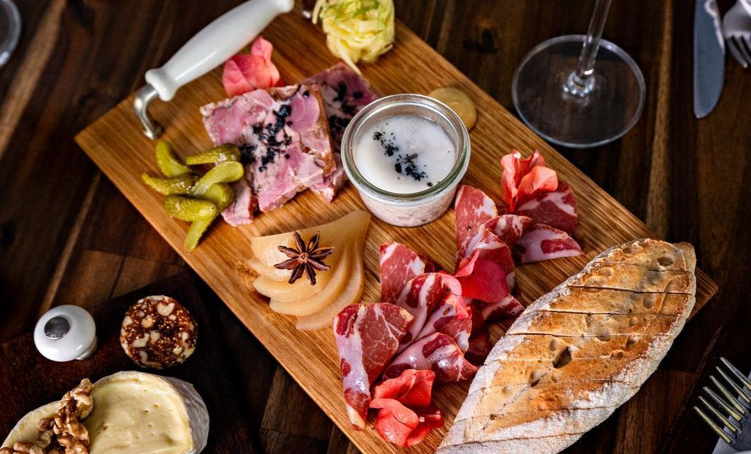 A wooden cutting board topped with meat and bread on a wooden table.