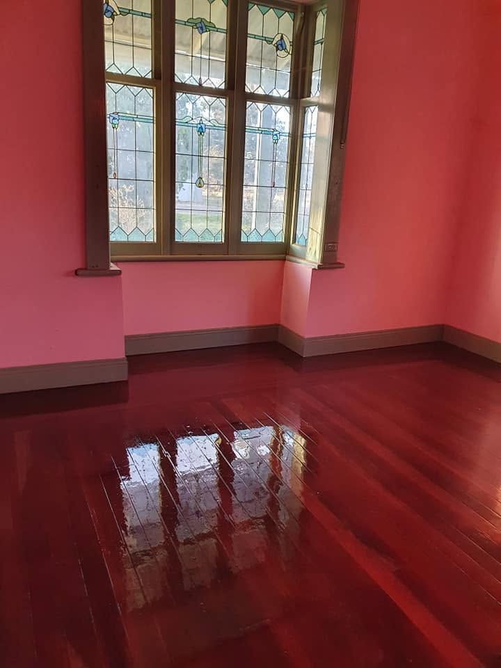 Empty pink room with a large window and glossy red wooden floor reflecting the light