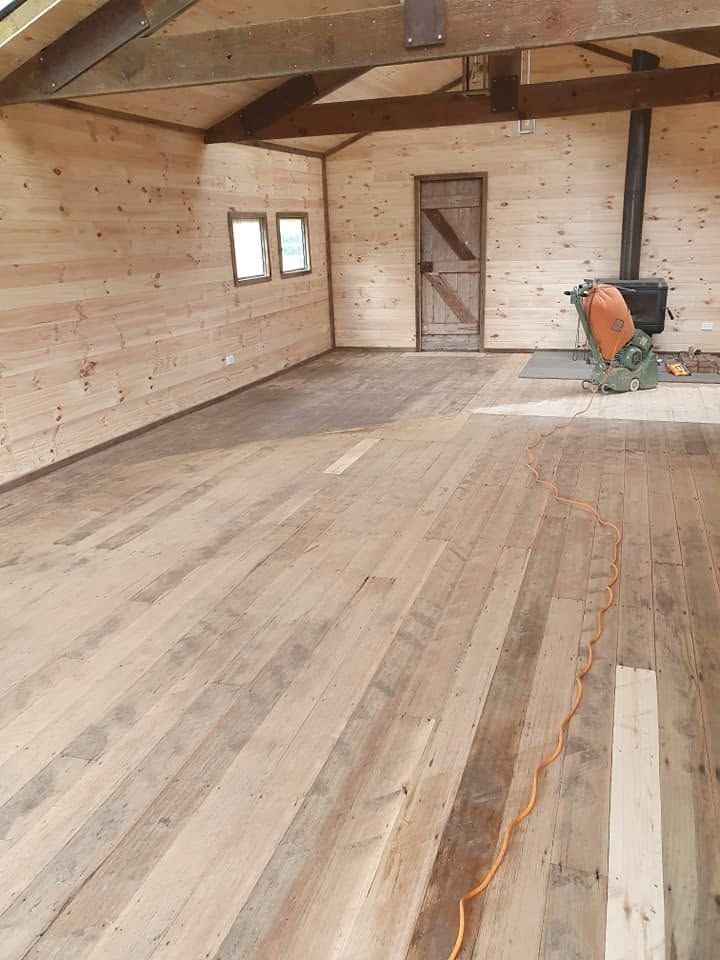 Empty wooden barn interior with plank floor, windows, and an orange wheelbarrow near the far wall