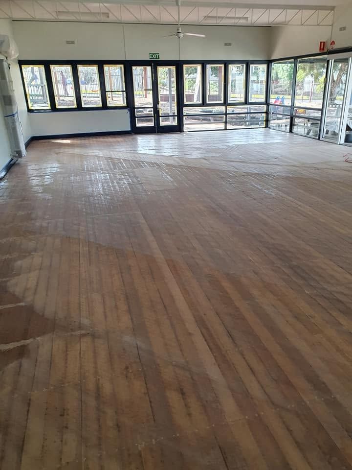 Empty room with worn wooden floor, windows along the wall, and glass entrance doors at the far end