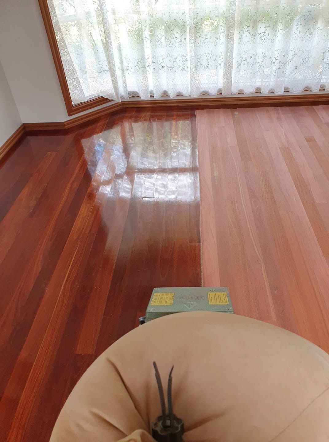 Polished wooden floor by a bright window, with the top of a beige chair in the foreground