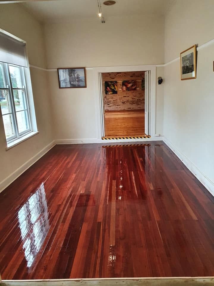 Empty white room with glossy red wood floor, windows, and an open doorway to another room