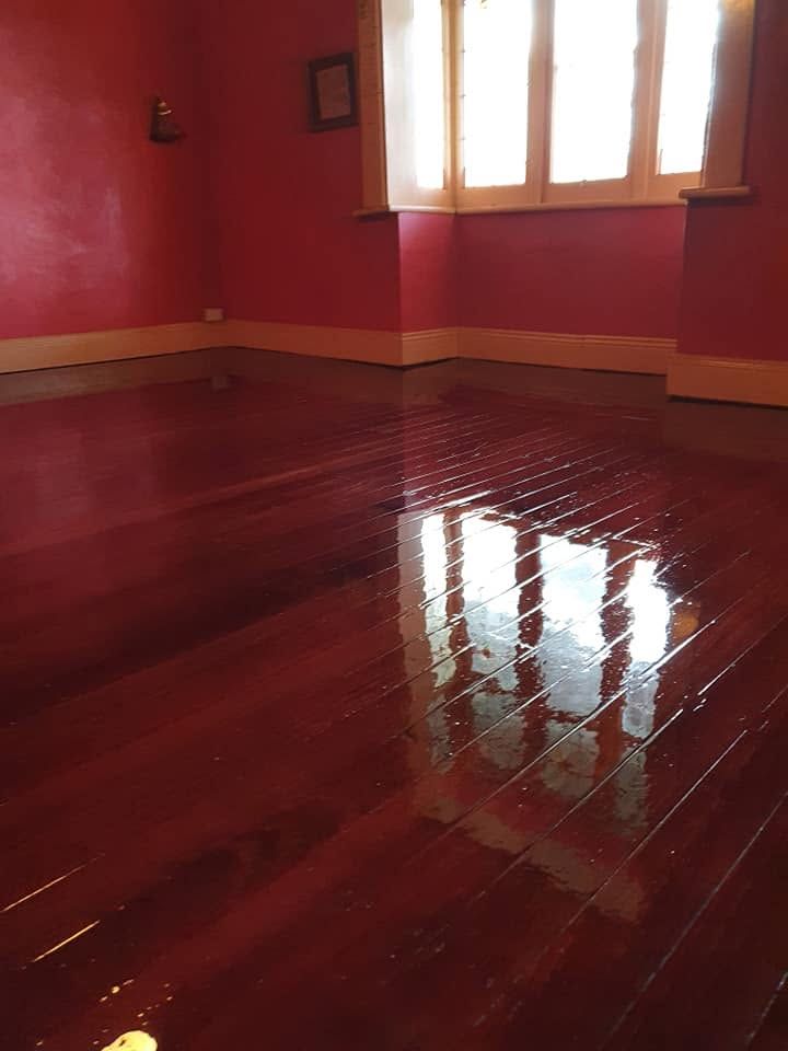 Empty room with red walls and glossy wooden floor reflecting light from a window.