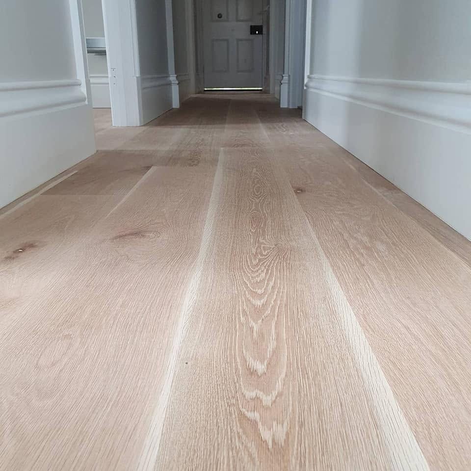Empty hallway with light wood flooring and white walls leading to a door.