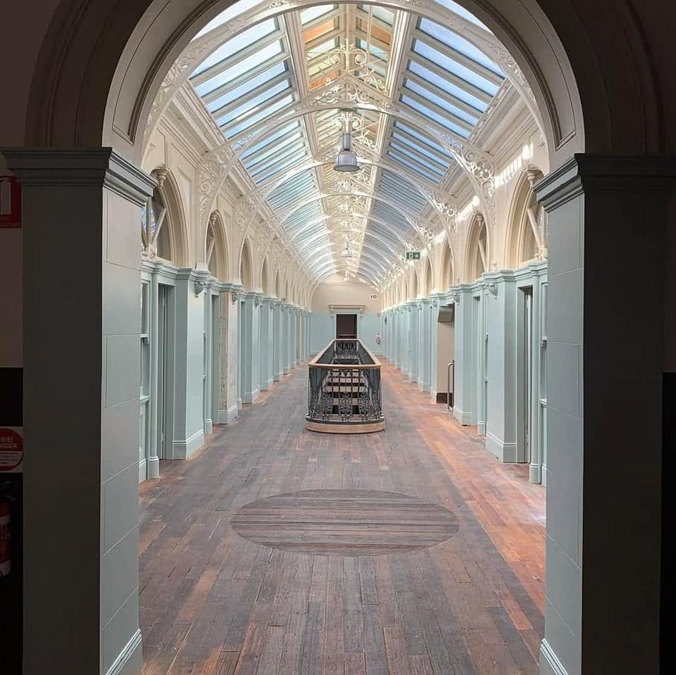 Bright museum hallway with glass ceiling, pale blue walls, and a central display case on wooden floors