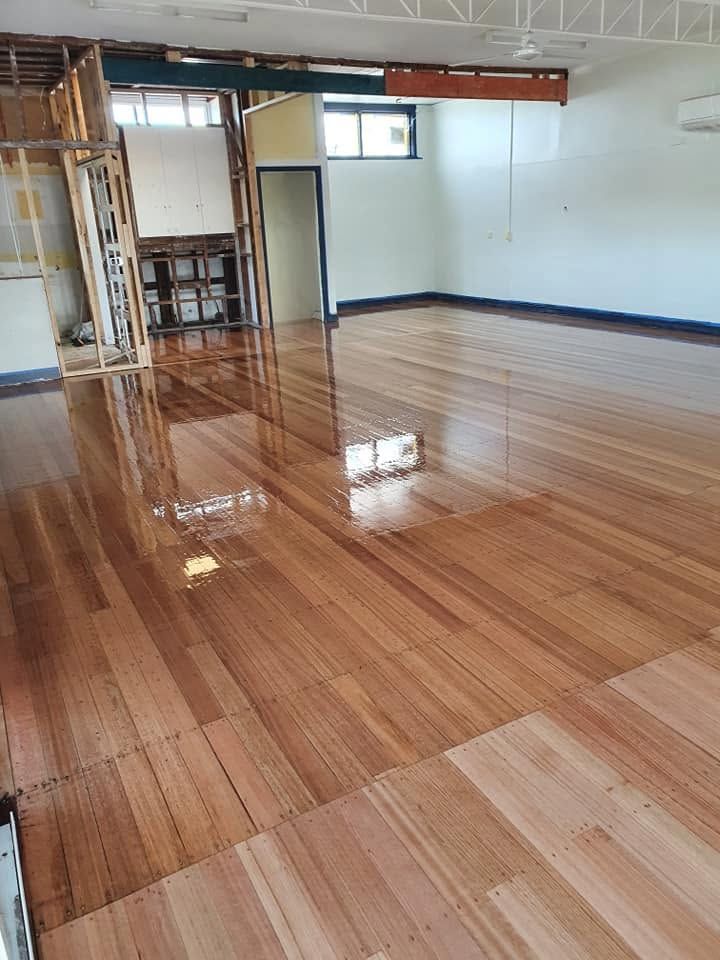 Empty room with glossy wooden floors, white walls, and exposed ceiling beams.