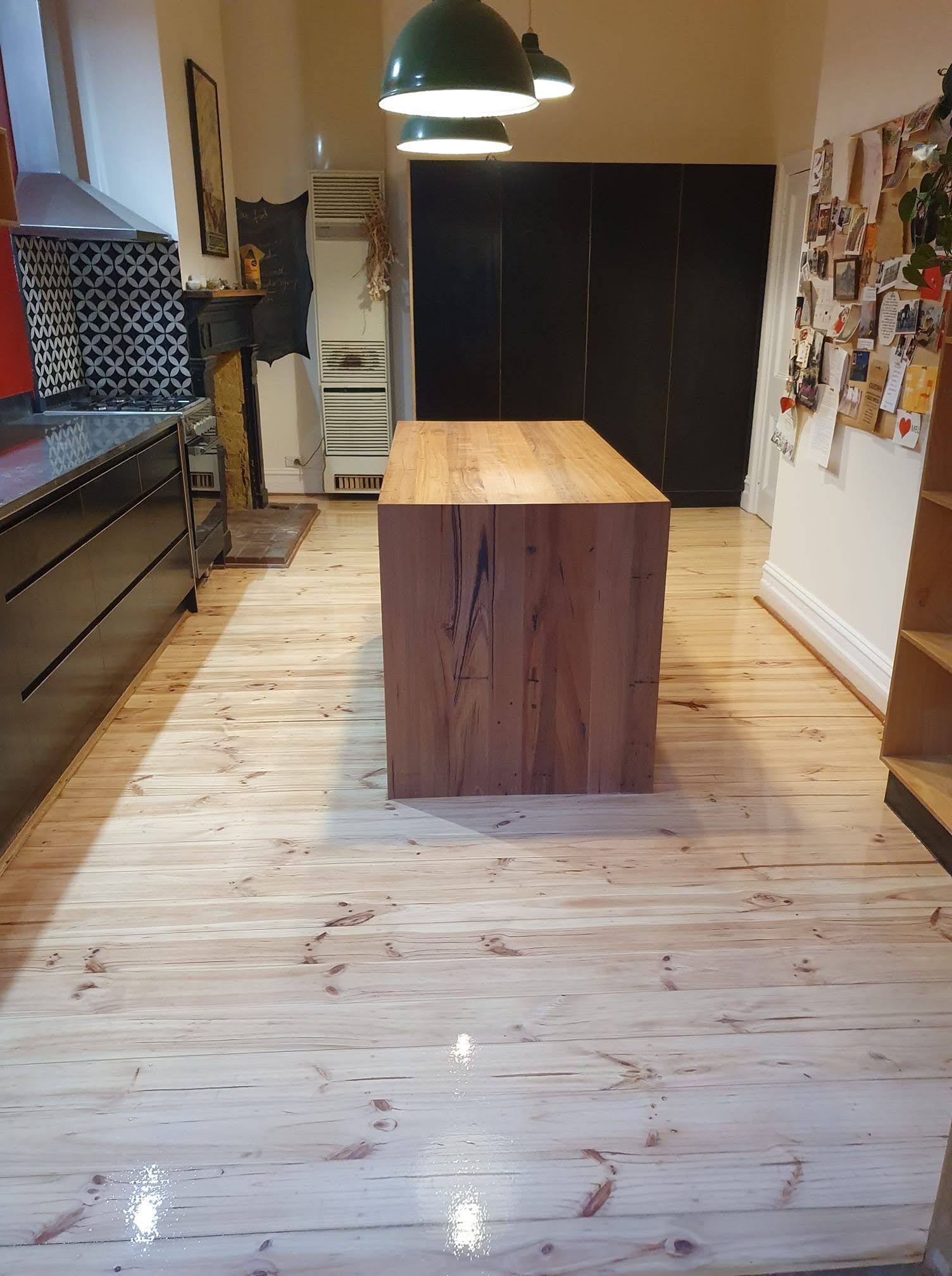 Bright kitchen with a wooden island, pendant lights, and black cabinets on a light wood floor