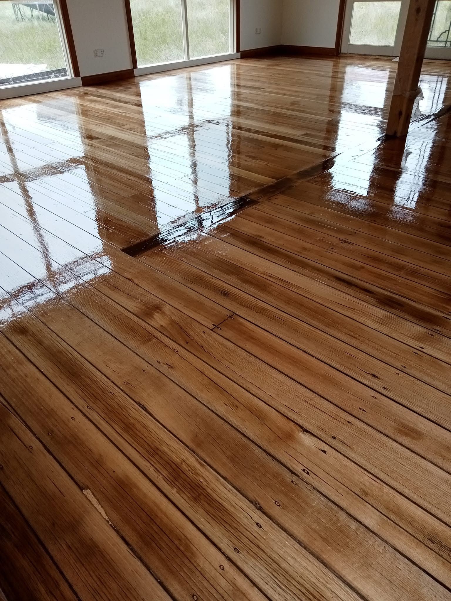 Glossy hardwood floor in an empty room with large windows reflecting light