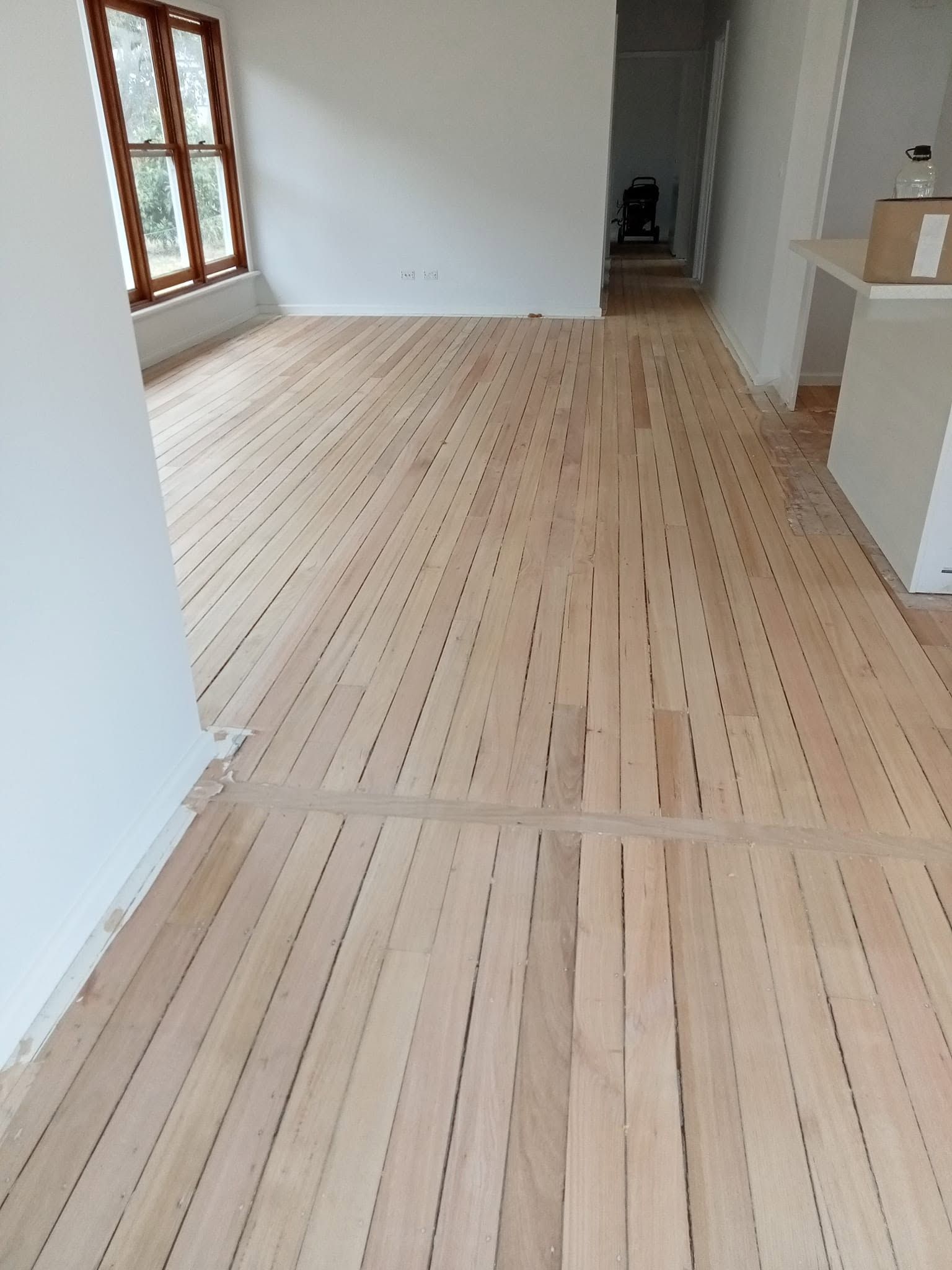 Empty room with light wood plank flooring and a window on the left.