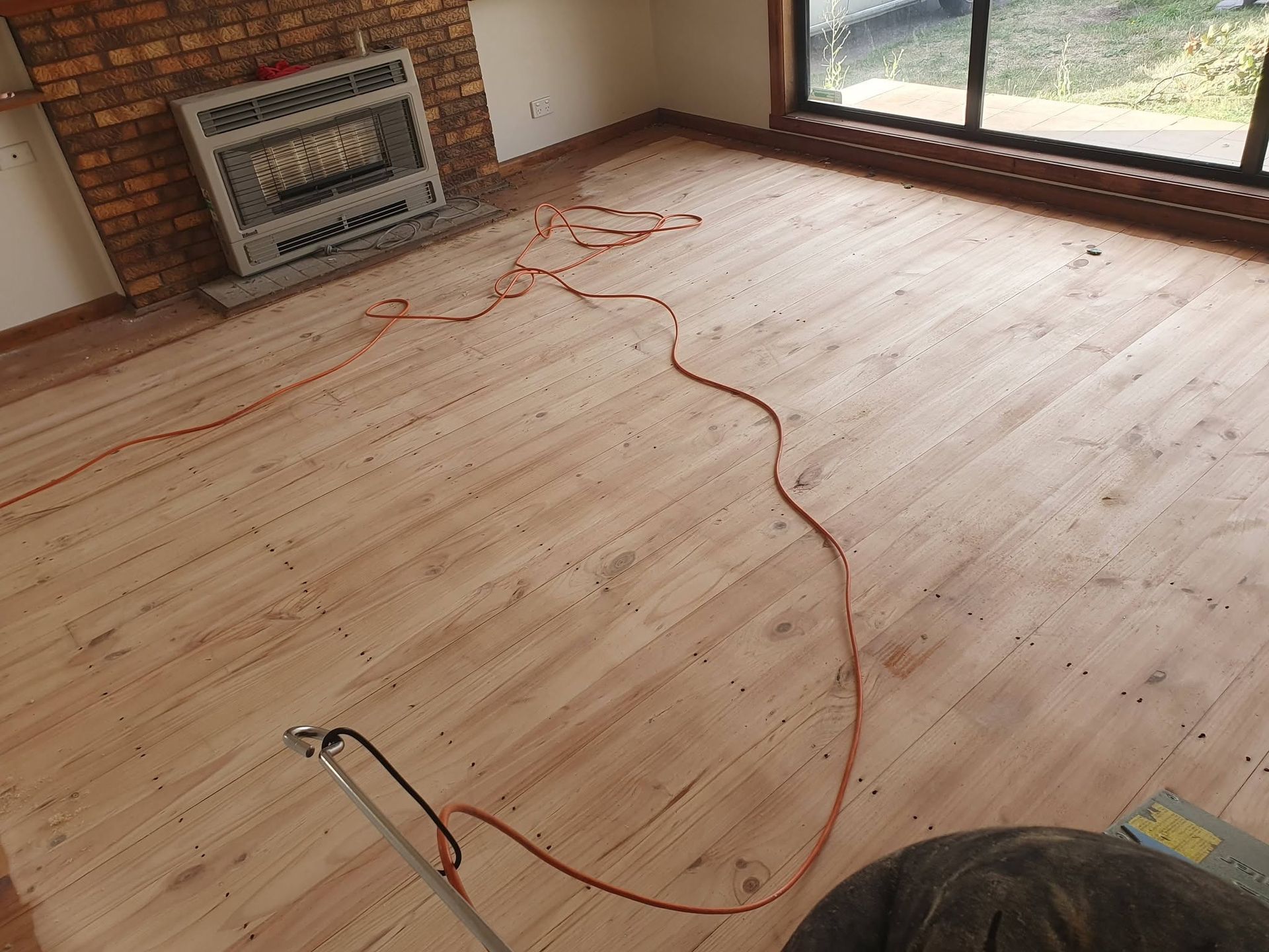 Sandable hardwood floor with an extension cord in an empty room near a large window.