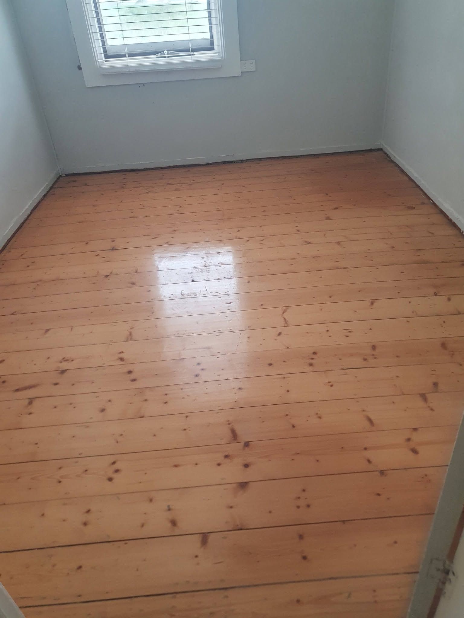 Empty room with light wood floor, white walls, and a small window.