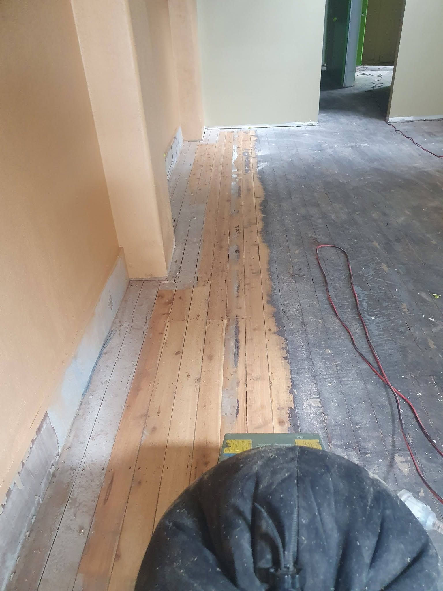 Hallway floor under renovation with wooden planks and cables beside a gray carpeted area