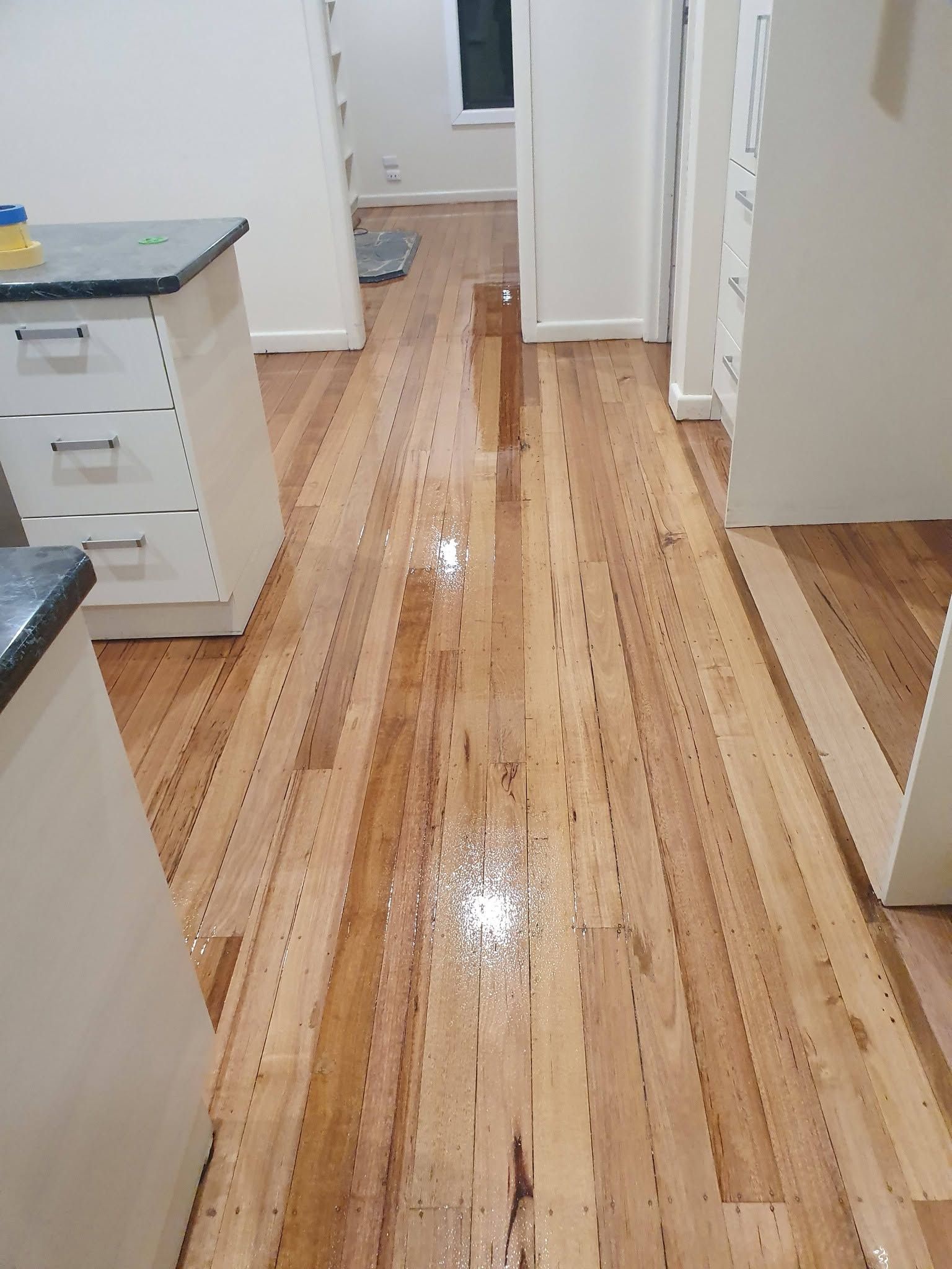 Narrow hallway with glossy wooden floor, white walls, and cabinets; wet patch or spill visible on the floor.