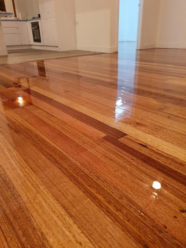 Shiny hardwood floor in a modern kitchen, reflecting light near white cabinets and a doorway.