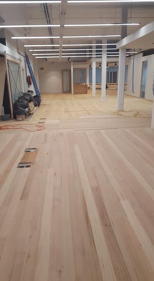 Empty indoor room with unfinished wood floor, exposed ceiling lights, and columns.