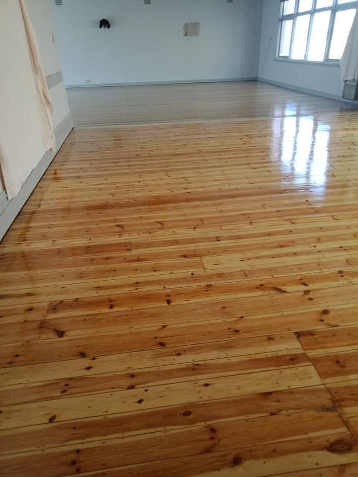Empty room with polished wooden floor and white walls, sunlight from windows on the right.