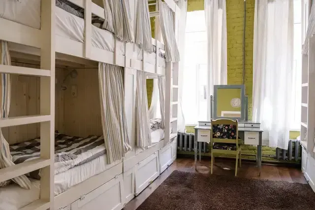 Bunk beds in a room with white curtains and a vanity. A green wall, wooden floor and a brown rug are also present.