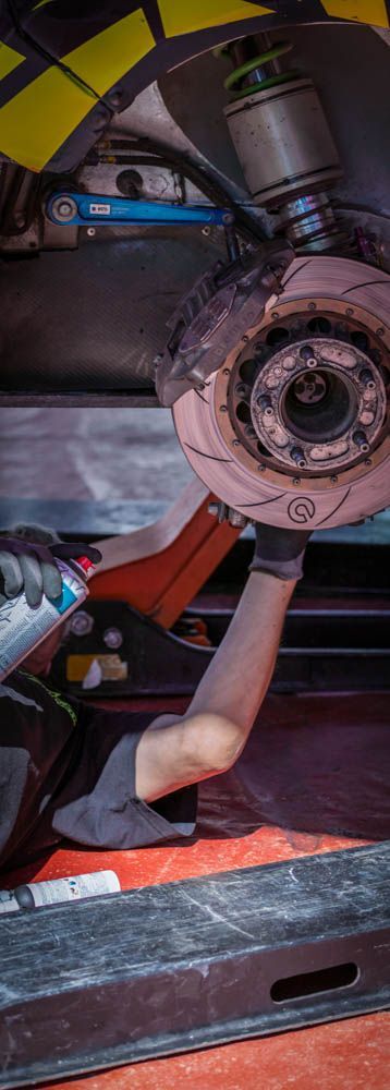 a mobile mechanic laying down on the ground providing brake services with a close up of the car's suspension and brake rotors