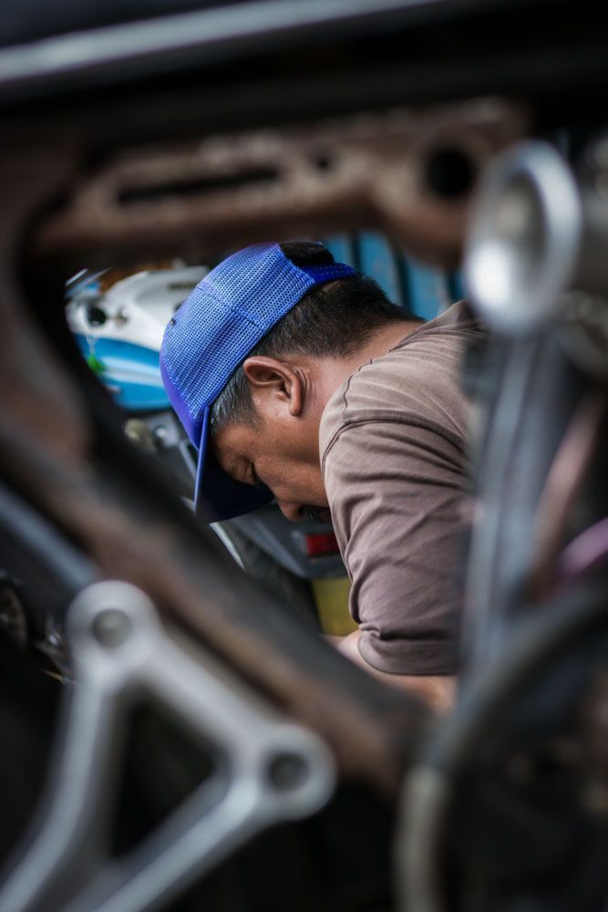 a close up of a car technician in a blue hat doing a vehicle analysis under the hood of family SUV
