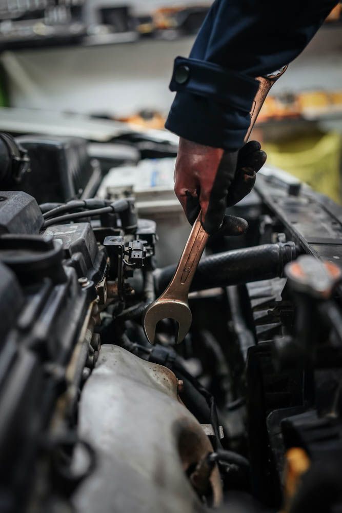 a close up of a car mechanic hand holding a wrench with a glove inside the vehicle's engine bay