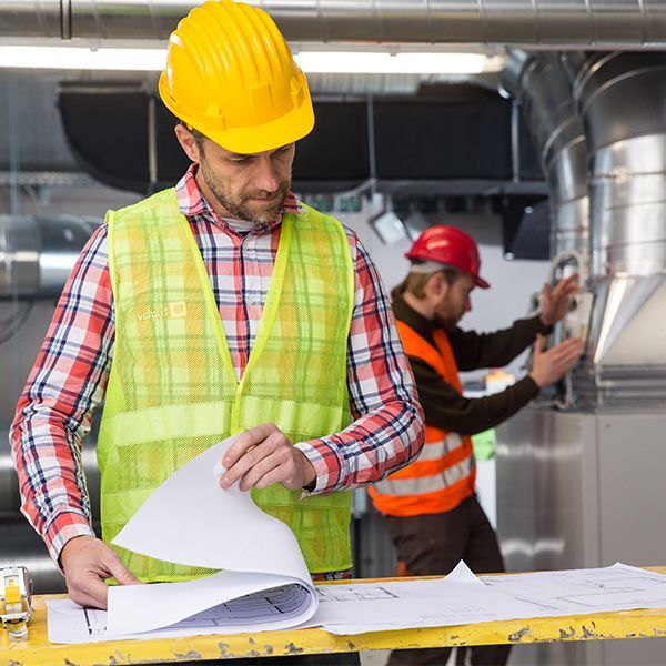 A man wearing a hard hat and safety vest is looking at a piece of paper.