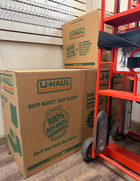 Stacked U-Haul cardboard boxes and a bright orange hand truck in a storage facility.