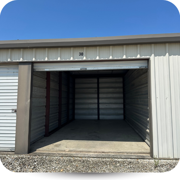 An open, empty self-storage unit with a concrete floor, metal walls, and a roll-up door, under a clear blue sky.