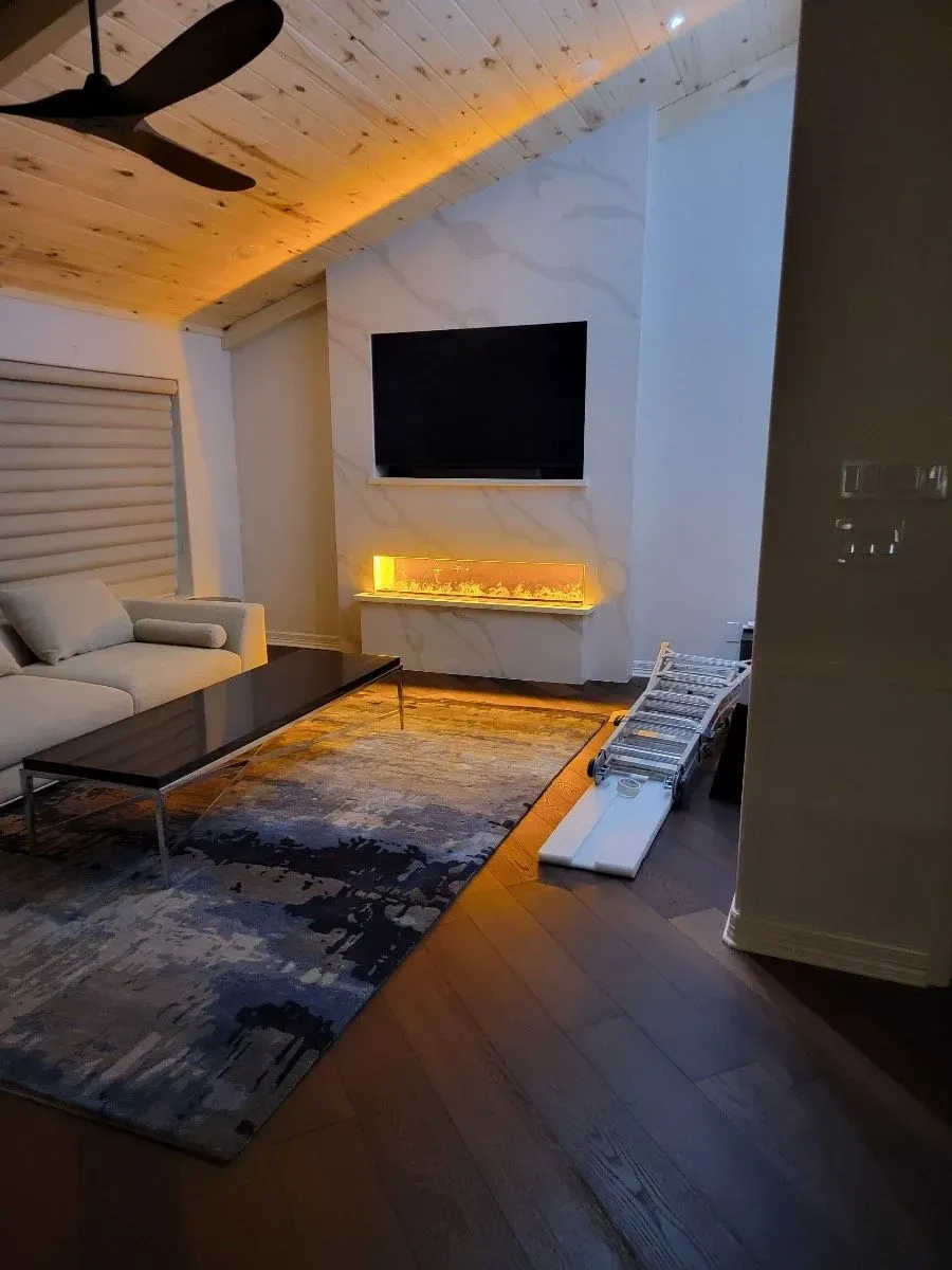 Living room with fireplace and large TV on a marble accent wall, hardwood floors, and a rug.