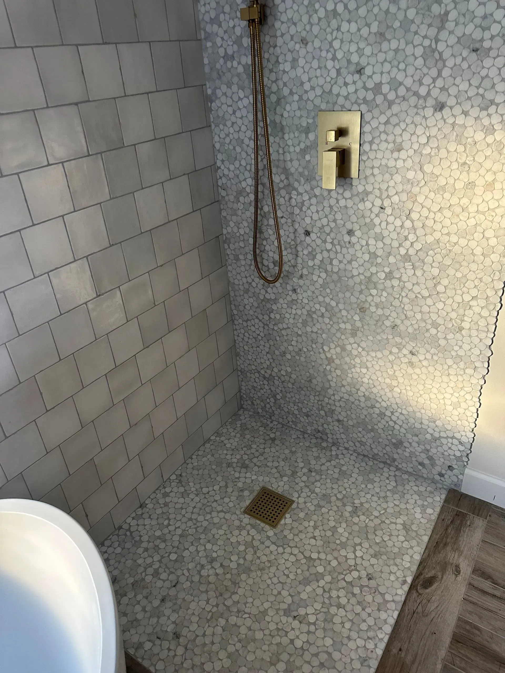 Shower with pebble tile and subway tile walls, brass fixtures, and a drain.