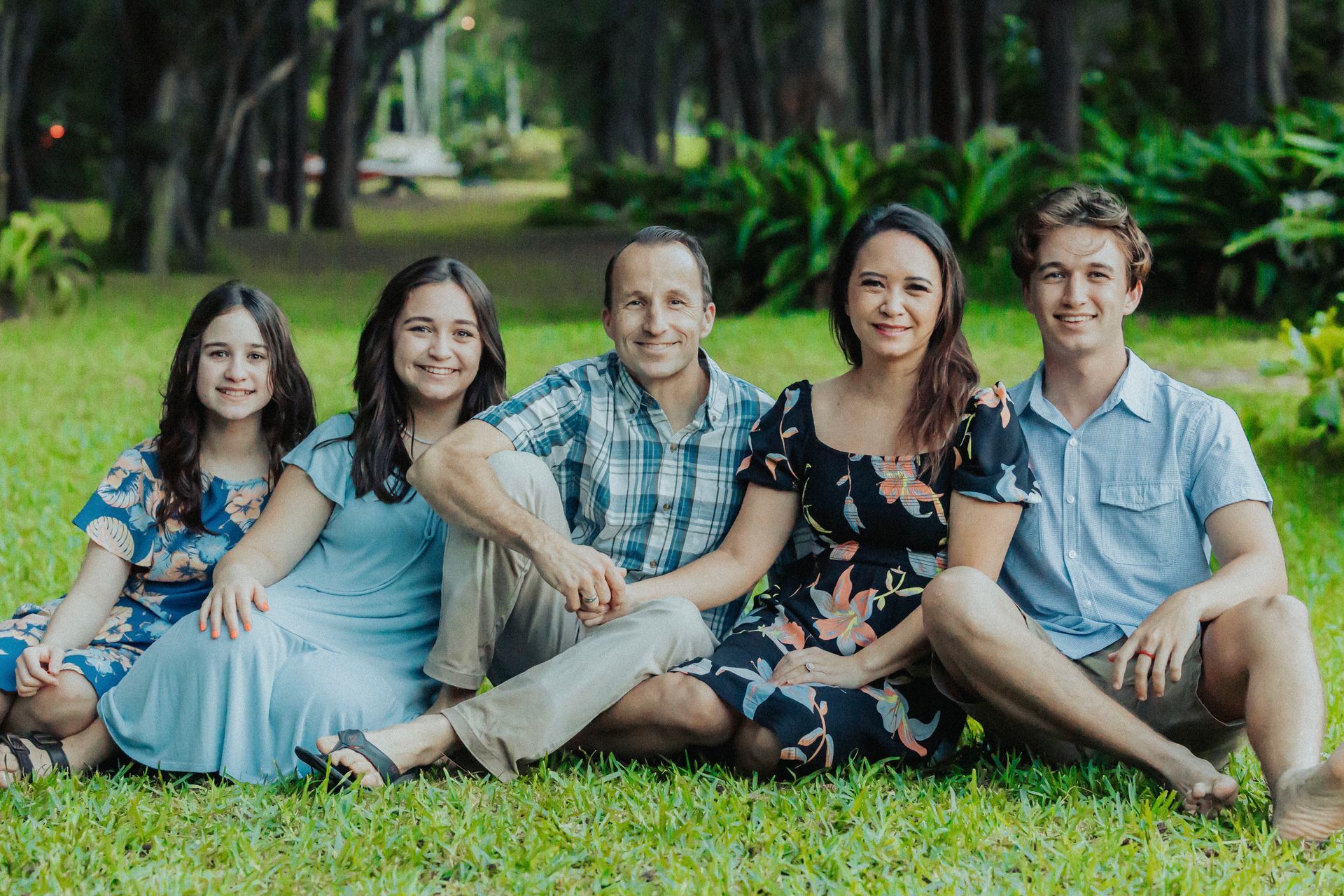 A family is posing for a picture while sitting on the grass in a park.