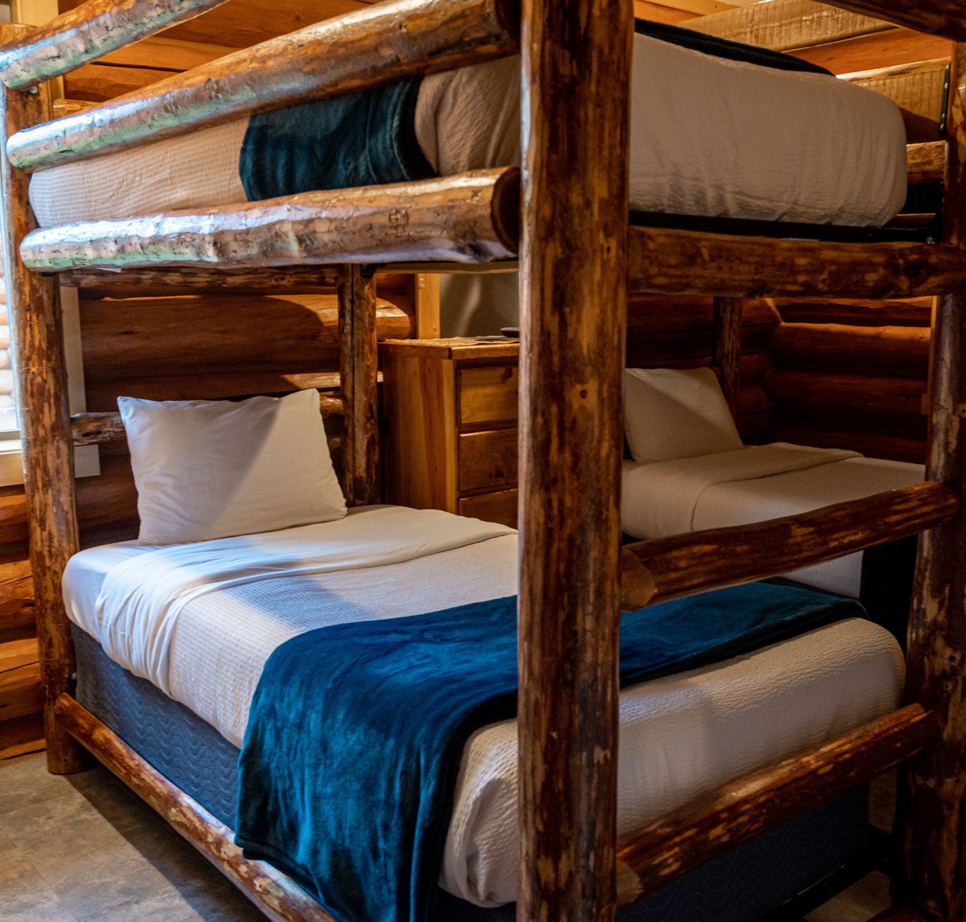 A bunk bed with a blue blanket on it in a log cabin.