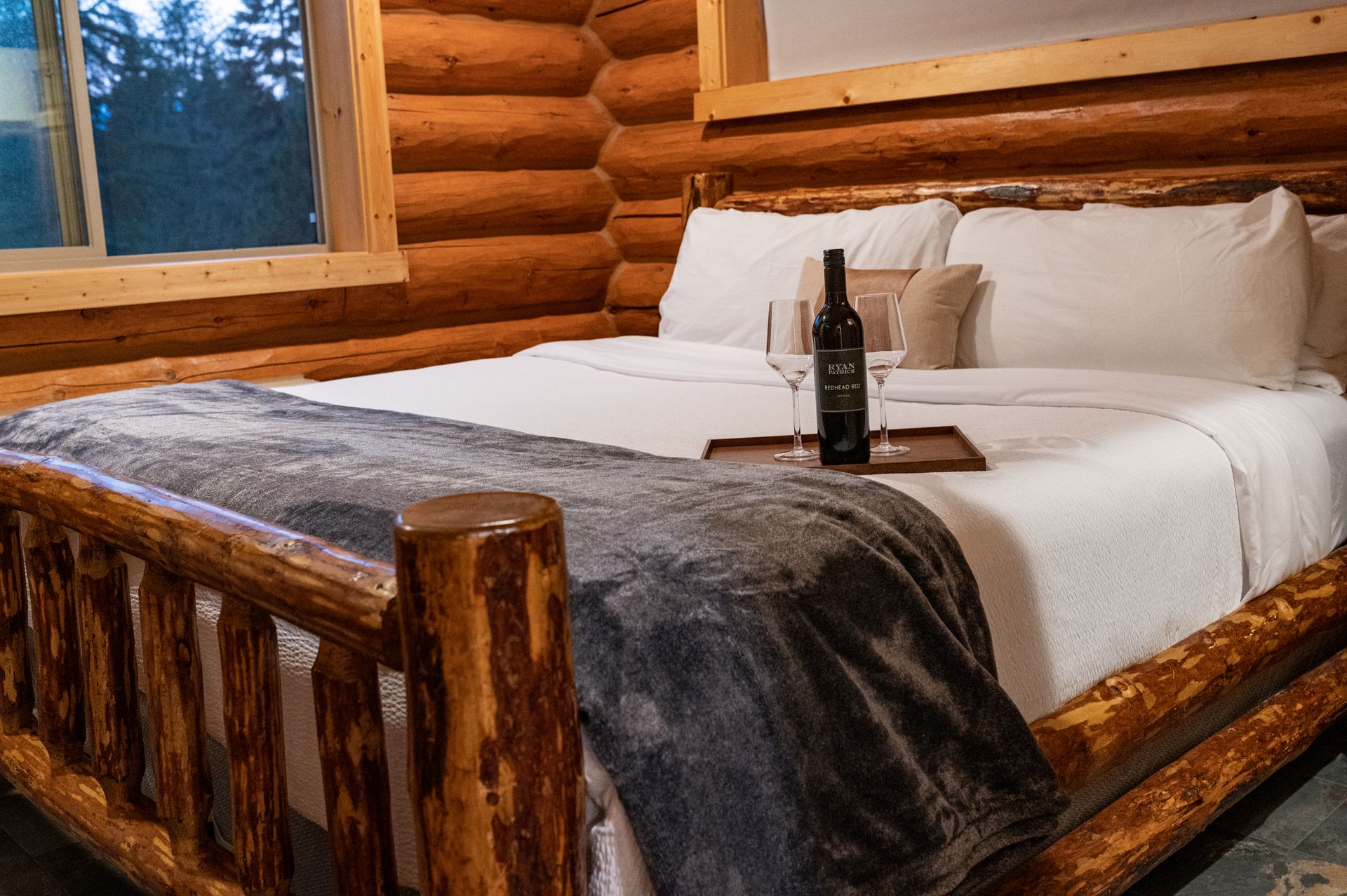 A bed in a log cabin with a bottle of wine on it.