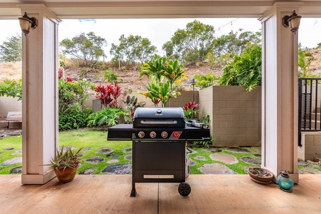 A grill is sitting on a patio next to a lush green yard.