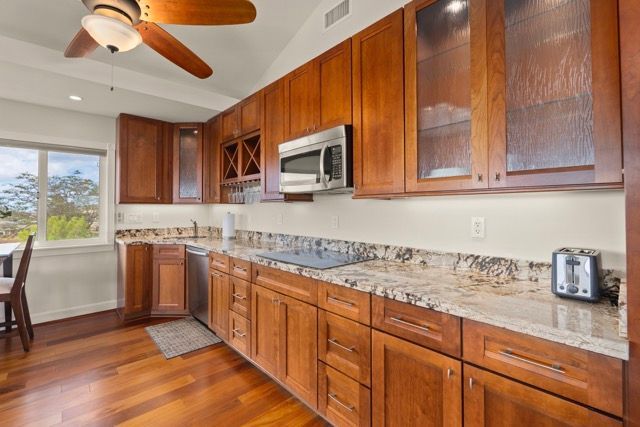 A kitchen with wooden cabinets , granite counter tops , stainless steel appliances and a ceiling fan.
