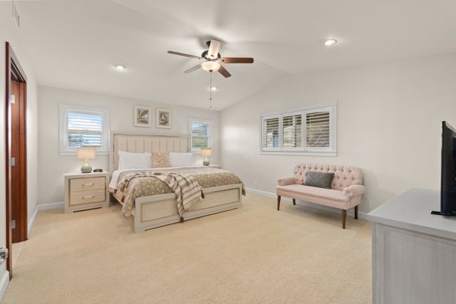 A bedroom with a large bed , a couch , a television and a ceiling fan.