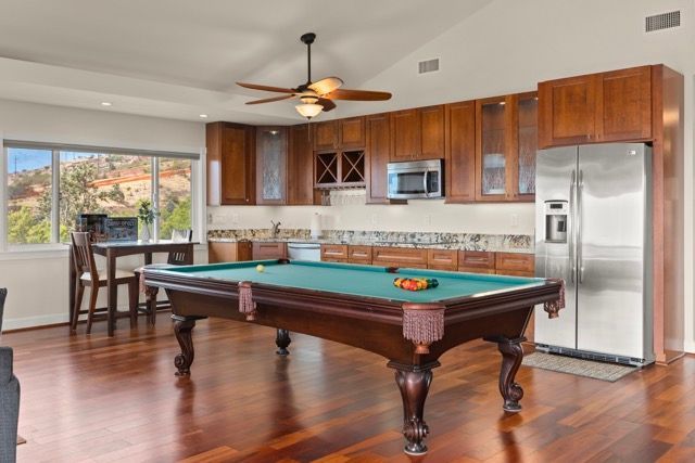A pool table in a living room next to a kitchen.