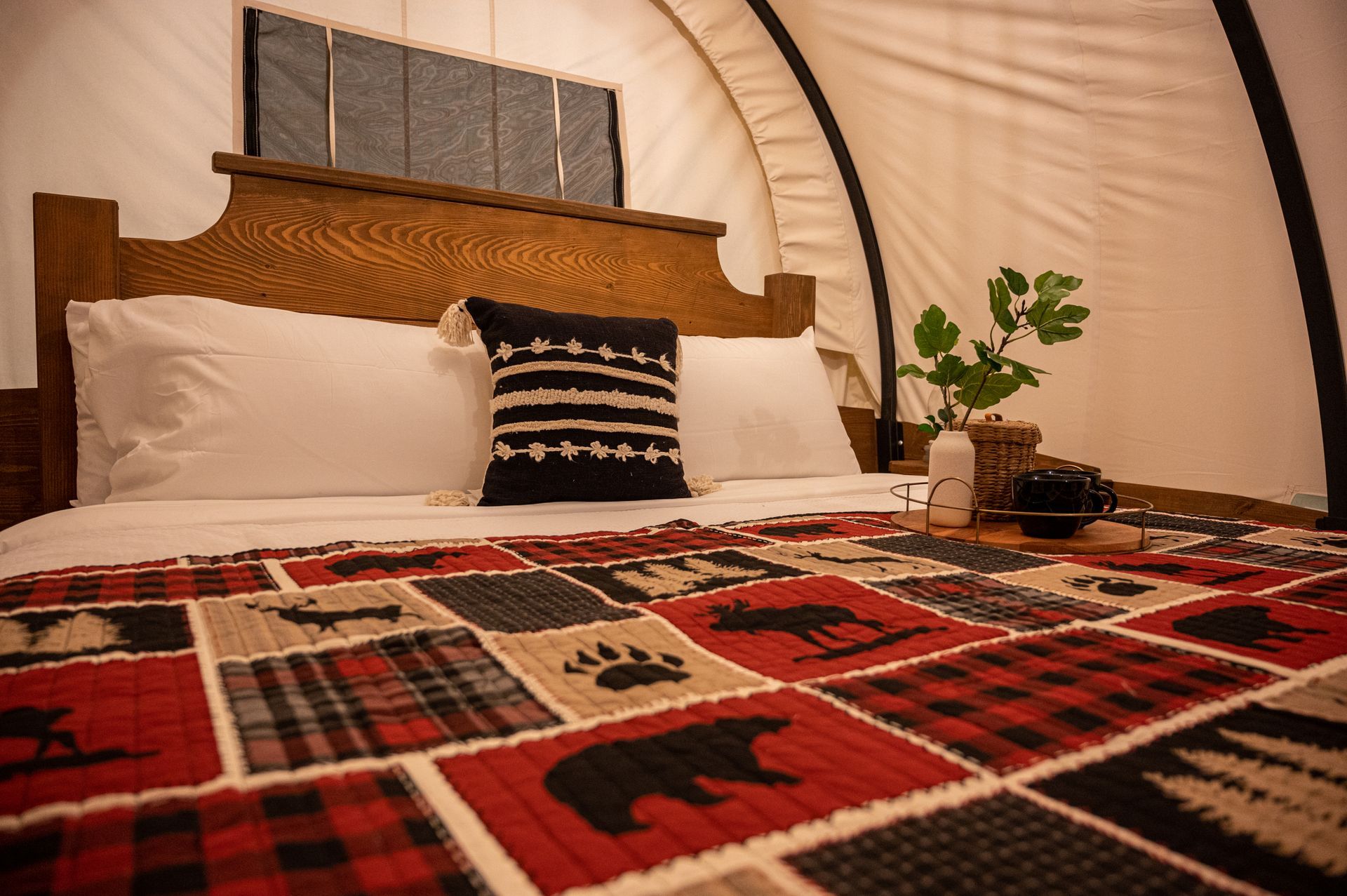 A bed with a plaid blanket and a pillow on it in a tent.