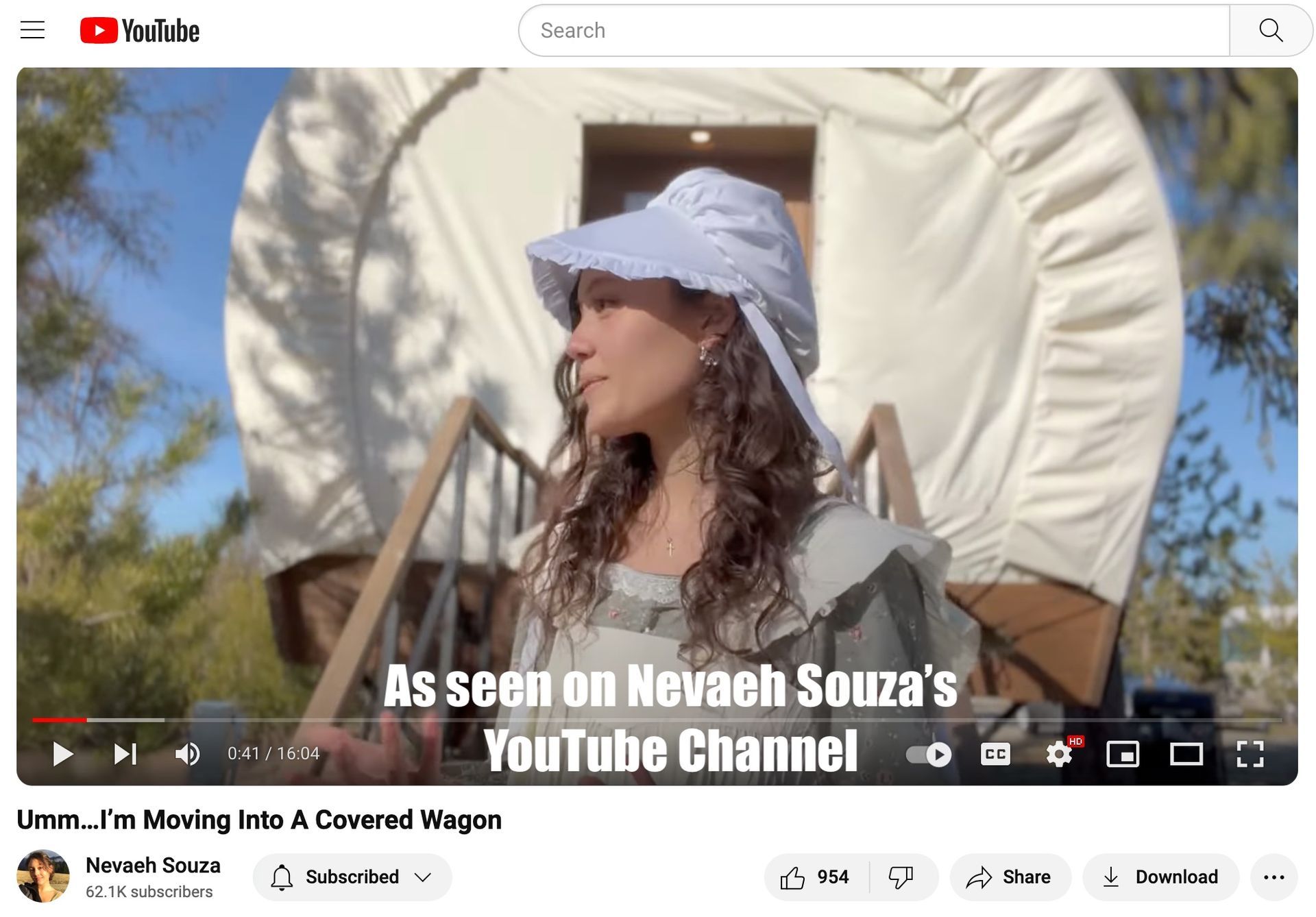 A woman in a hat is standing in front of a covered wagon.