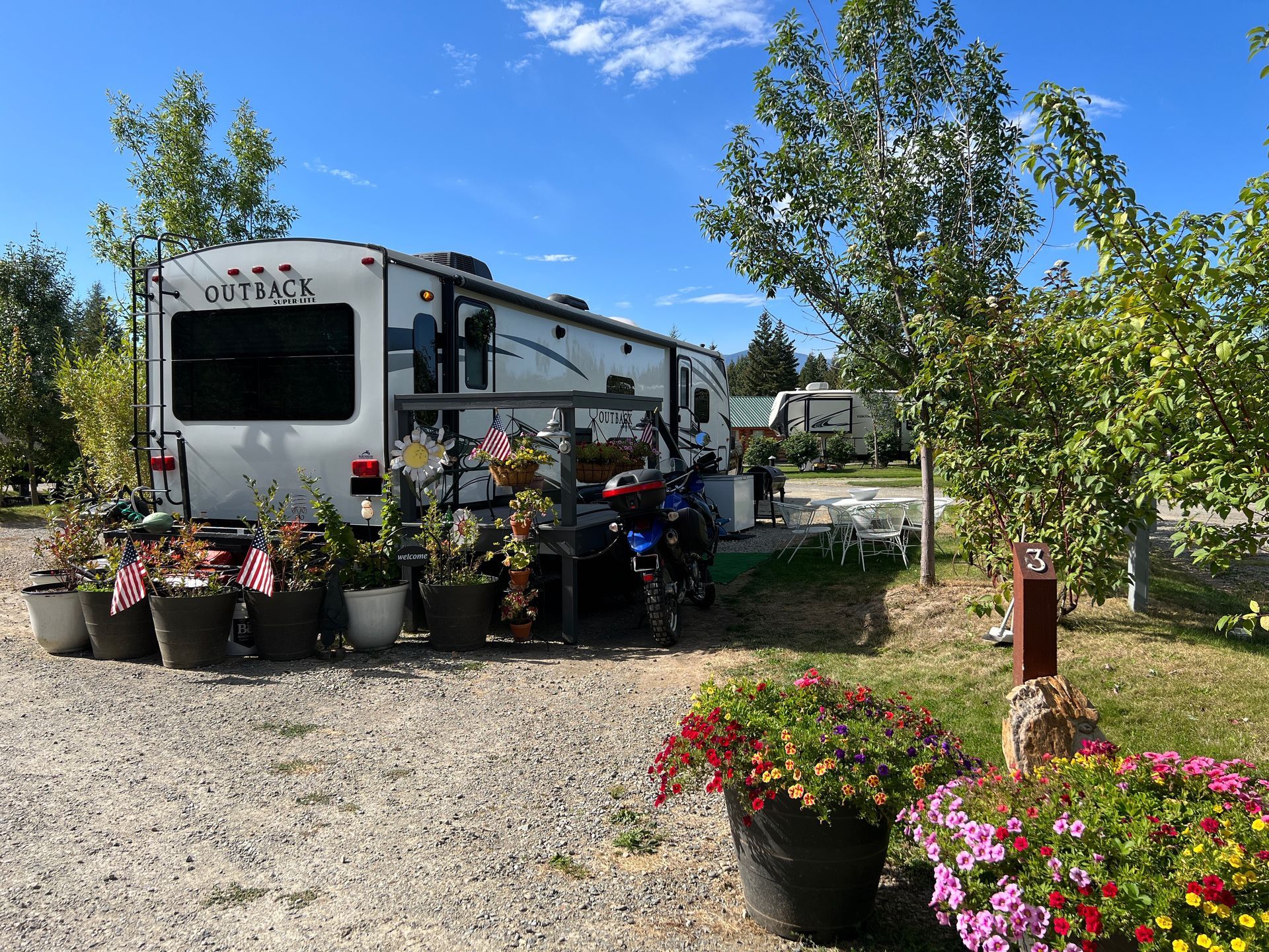 A rv is parked in a gravel lot surrounded by potted plants and flowers.
