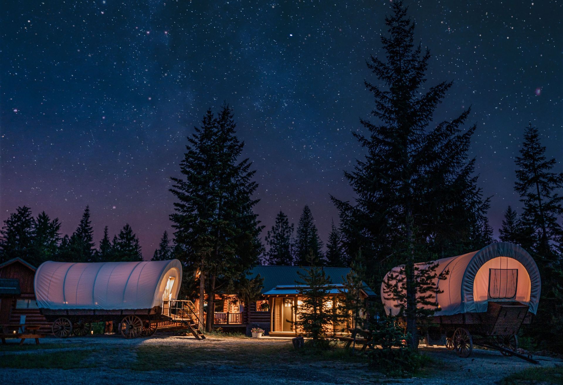 A covered wagon is parked in front of a house under a starry night sky.