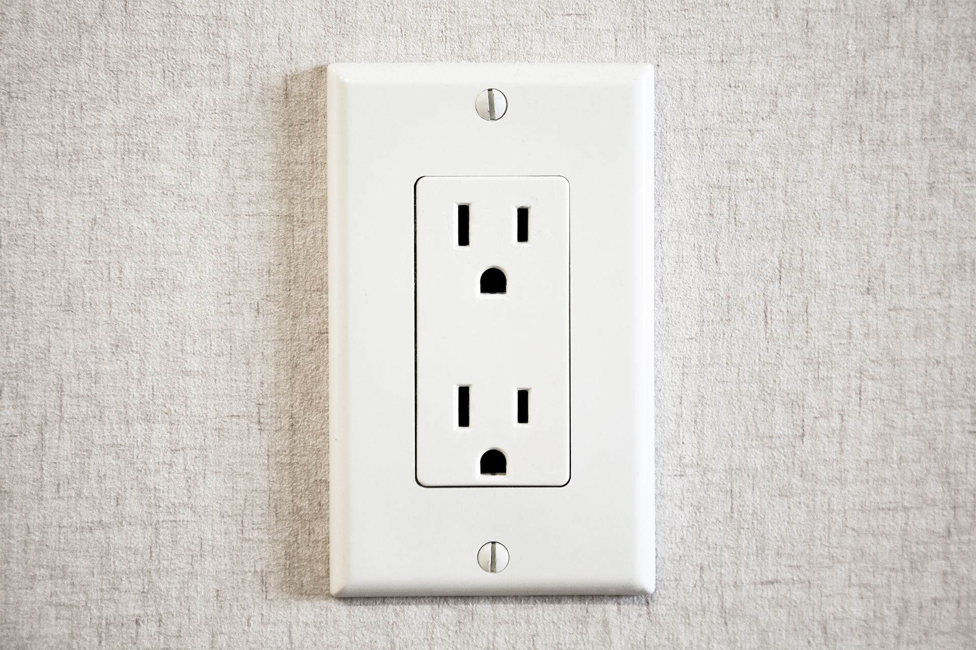 White electrical wall outlet on a beige textured wall.