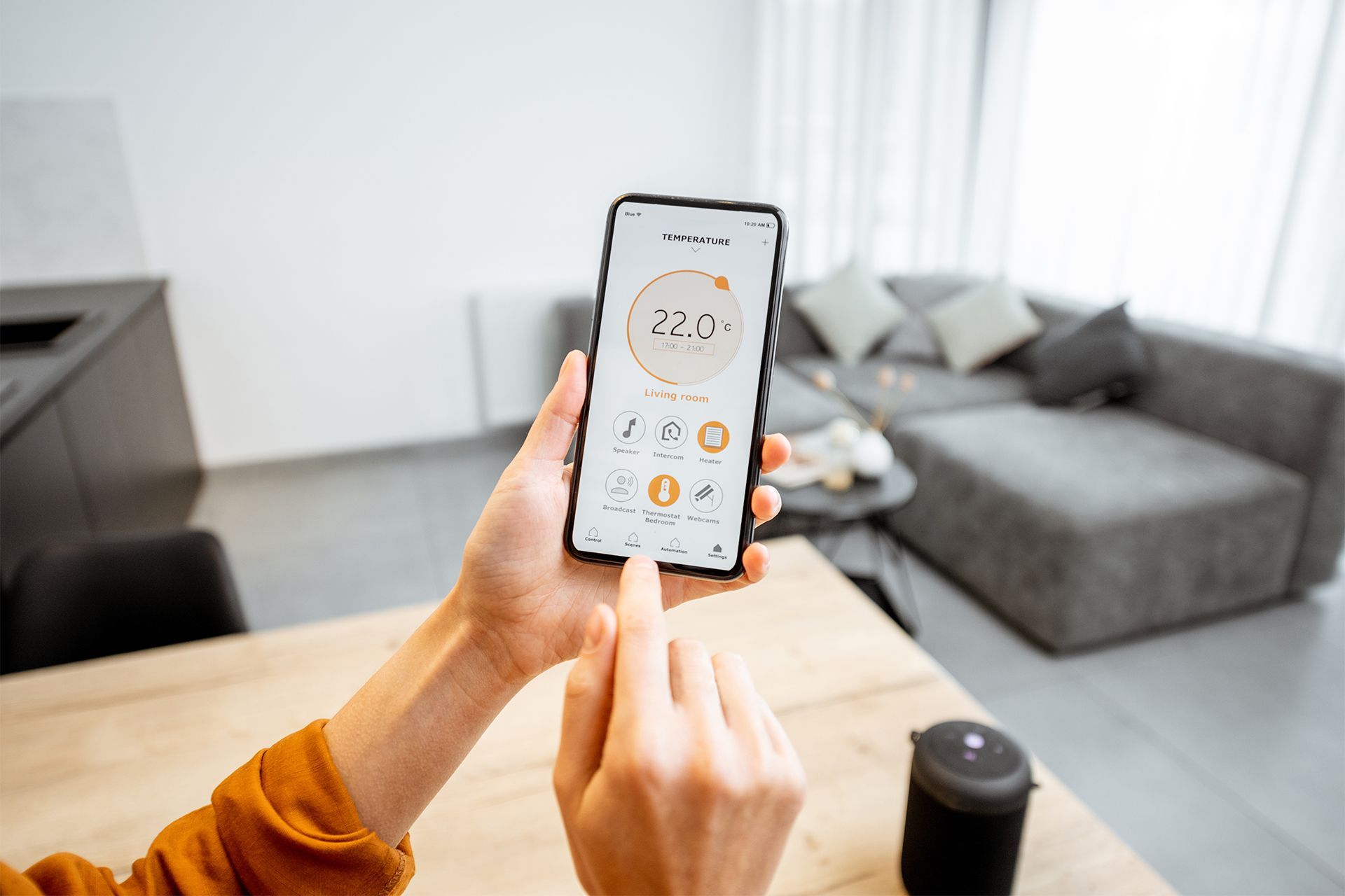 Hands holding a smartphone with a weather app open in a bright living room.