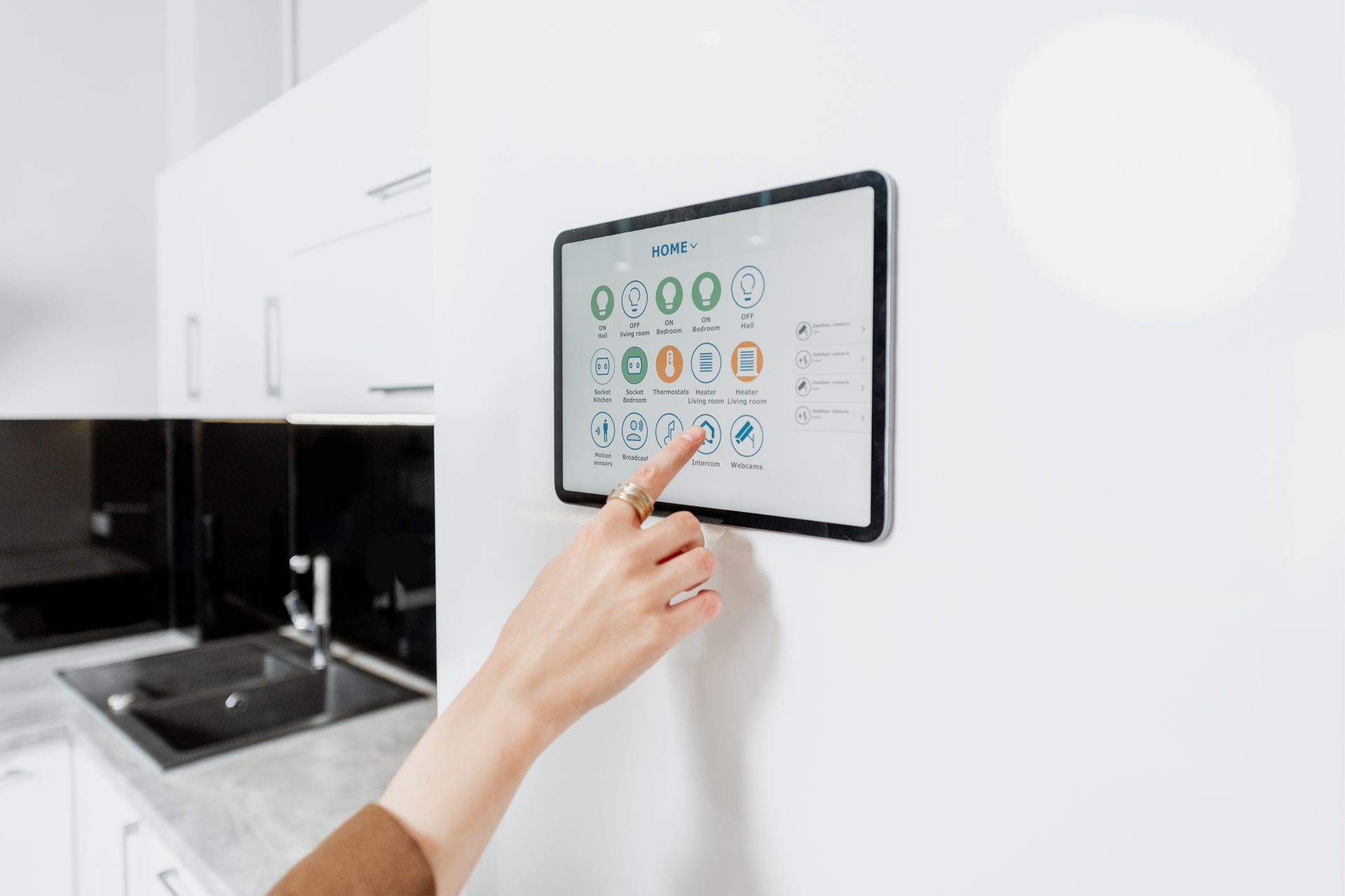 Hand tapping a touchscreen control panel in a modern white kitchen.