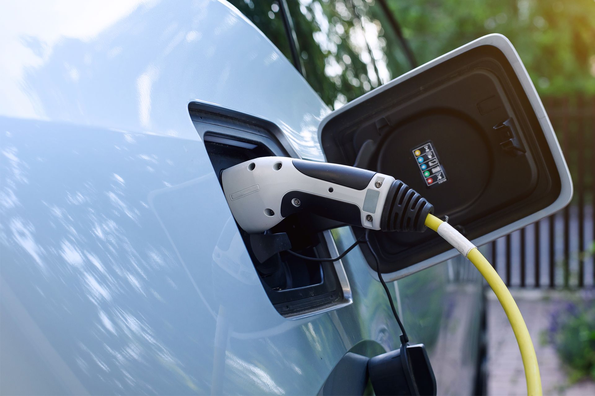 Electric car charging port connected to a cable on a blue vehicle outdoors.