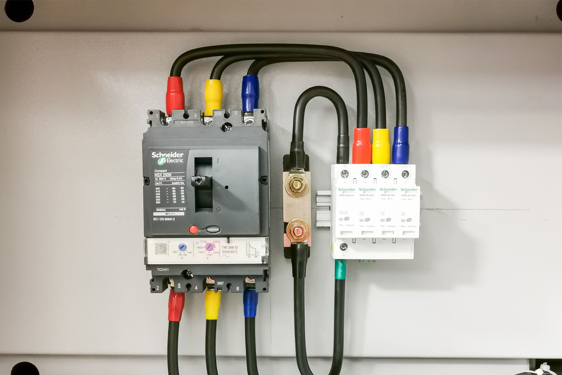 Electrical control panel with colored cables and breakers mounted on a wall.