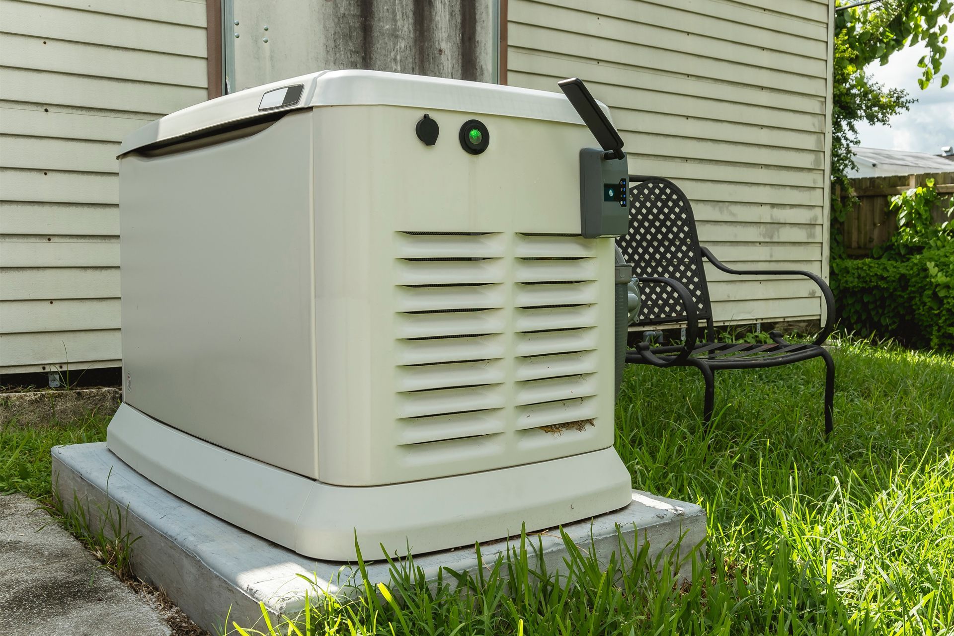 White backup generator beside a house on a concrete pad in a grassy yard.