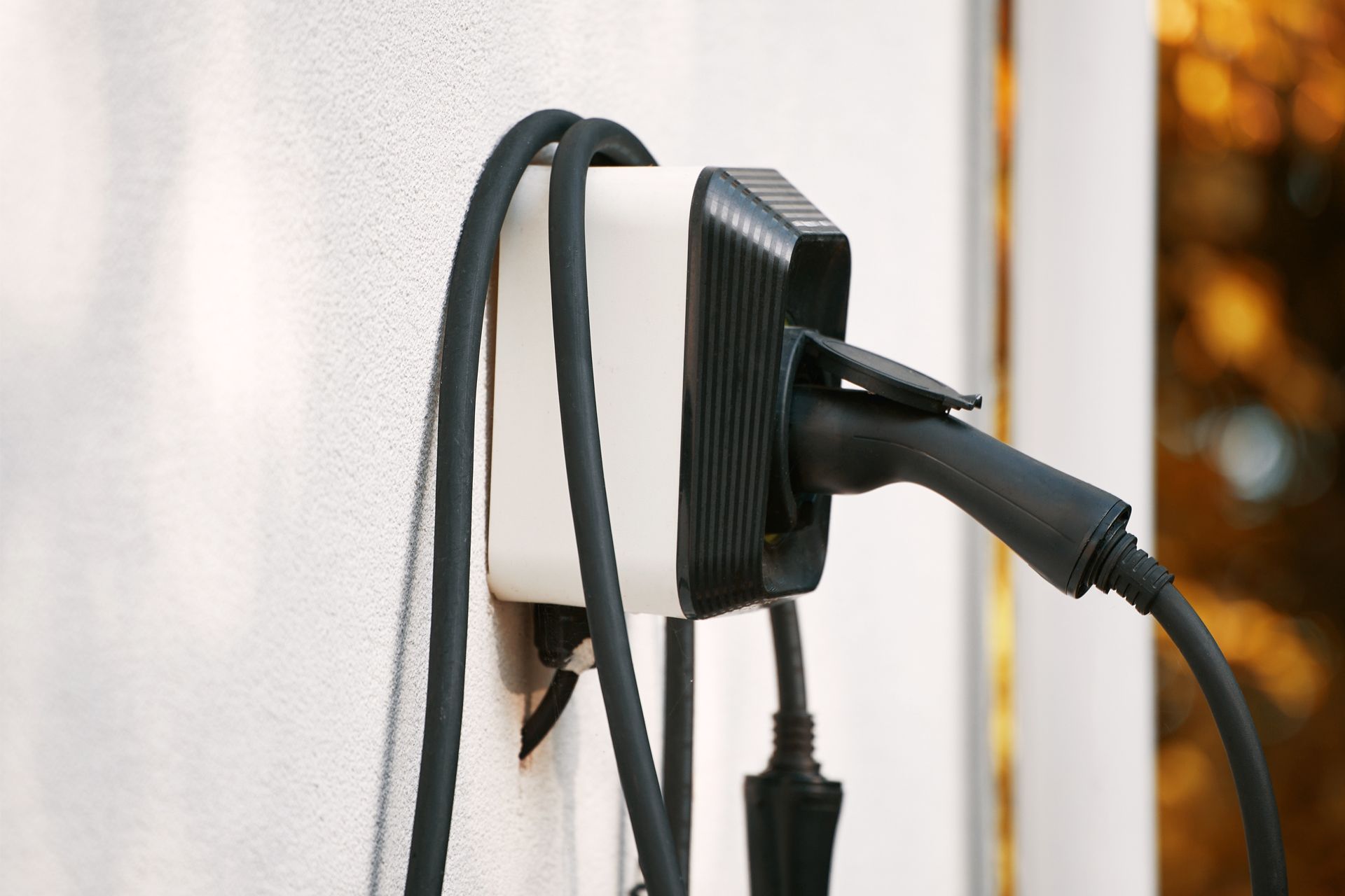 Black charger plugged into a wall-mounted power strip with a cable hanging down.
